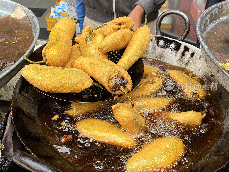 一个不认识的人在煮绿辣椒油饼(mirch pakora)，在大油锅里油炸，印度街头小吃摊贩，印度街头小吃摊档，不健康的饮食，高架视野，重点在前景